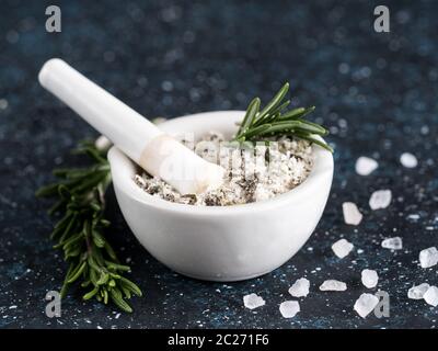 Nahaufnahme von Mörser und Stößel mit Meersalz duftenden Rosmarin und Zitronenschale. Meersalz duftende Kraut Rosmarin auf dunkelblauem Hintergrund. Duftendes Salz Stockfoto