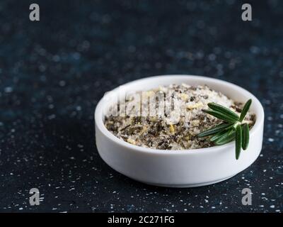 Meersalz duftende Kräuter Rosmarin und Zitronenschale. Meersalz mit aromatischem herbin kleine Schüssel auf dunkelblauem Hintergrund. Duftendes Salz und Pfefferkuschen. Kopie sp Stockfoto