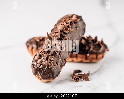 Hausgemachte eclairs mit Schokolade auf weißem Hintergrund. Nahaufnahme der leckeren, gesunden profitroles mit Schokoladenüberzug Stockfoto