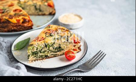 Zucchini Pie und Zutaten auf grauem Hintergrund, kopieren Raum. Stück köstliche herzhafte Torte mit Zucchini, Tomaten, Kräutern und Käse. Idee und Rezept Stockfoto