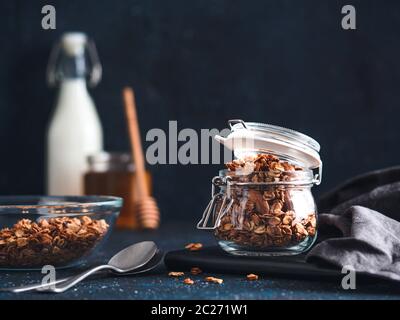 Hausgemachtes Müsli in Glas Glas auf dunklen Tisch. Zutaten für gesundes Frühstück - Müsli, Milch und Honig. Kopieren Sie Platz für Text. Low Key. Stockfoto