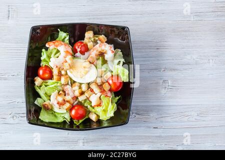 Blick von oben auf die Caesar Salat mit Garnelen in schwarz Schüssel auf grau Holztisch mit Copyspace Stockfoto