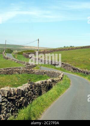 Eine Kreuzung auf einer gewundenen schmalen Landstraße, die von Trockenmauern in hügeligen yorkshire-Dales-Landschaft mit blauem Sommer sk begrenzt wird Stockfoto