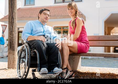 Mann im Rollstuhl und Frau, die im Sommer auf einer Bank Snacks isst Stockfoto