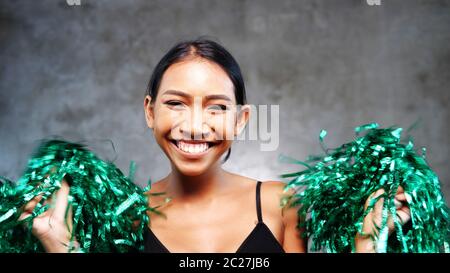 Porträt von schönen jungen lächelnden Mädchen mit grünen Cheerleader Pom-Poms über Betonwand Hintergrund Stockfoto