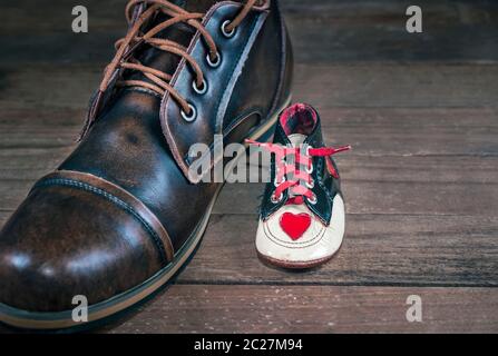 Die Neugeborenen Schuh neben Erwachsenen Schuh ist ein und dieselbe Person. Konzept Bild des Wachstums, des Alterns und der Entwicklung von Mode und Design. Stockfoto