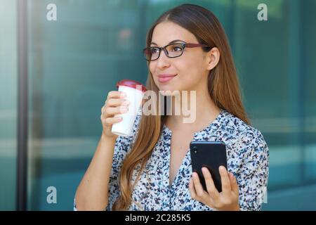 Porträt eines lächelnden business Frau mit Handy während die Tasse Kaffee, bevor sie an die Arbeit zu gehen und Wegsehen. Stockfoto