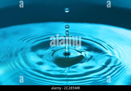 Wassertropfen, der in Wasser fällt und so eine perfekte konzentrische Kreisfläche darstellt. Abstrakter blauer Hintergrund. Stockfoto