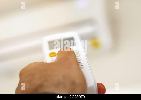 Nahaufnahme einer Hand, die die Temperatur der Klimaanlage mit der Fernbedienung anpasst Stockfoto