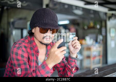 Asiatische Hipster Mann halten Kreditkarten und mit Mobiltelefonen für Online-Shopping. Stockfoto