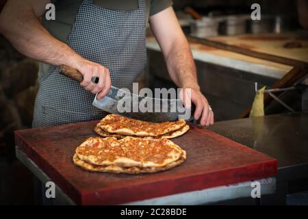 Gebackene Lahmacun ist ein rundes, dünnes Stück Teig, gekrönt mit Hackfleisch (am häufigsten Rind oder Lamm), gehacktem Gemüse und Kräutern. Mann schneidet lahmacun. Stockfoto