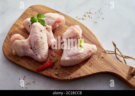 Teile von rohem Huhn mit Kräutern und Gewürzen und red hot chili peppers auf einer hölzernen Schneidebrett über einem weißen Marmor in einer Ansicht von oben Stockfoto