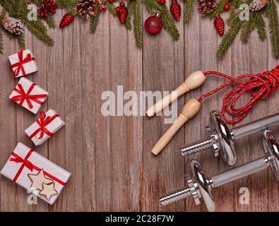 Hanteln, Springseil, Geschenkboxen, Tannenzweige und Weihnachtsschmuck auf Holzhintergrund. Draufsicht mit Kopierbereich. Neujahr, Weihnachten. Fitnes Stockfoto