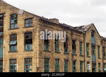 Das kaputte Dach und die kaputten Fenster in einem großen, ausgebrannten alten Industriegebäude nach einem Brand Stockfoto