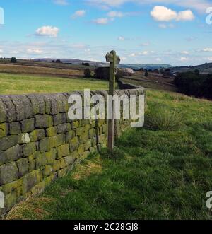 Die offene Landschaft mit Richtung neben einer Trockenmauer mit grünen Feldern und mooland in der Ferne in Yorkshire, England Stockfoto