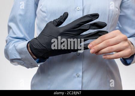 Junge Frau in blauer Bürobluse zieht vor den Eingriffen schwarze Latexhandschuhe aus. Nahaufnahme. Stockfoto