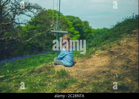 Ein kleiner Vorschulkinder sitzt auf einer Wiese mit einer Seilschaukel, die an einem Baum hängt Stockfoto