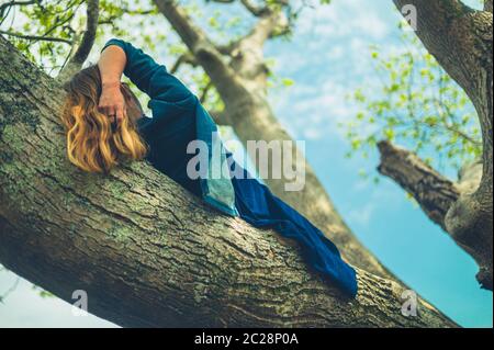 Eine junge Frau liegt auf dem Ast einer Esche Stockfoto