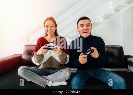 Glückliches junges Paar, sehr aufgeregt beim Spielen von Computerspielen mit Joysticks, sitzen auf der Couch, zu Hause. Stockfoto