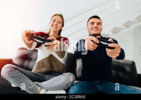 Glückliches junges Paar, sehr aufgeregt beim Spielen von Computerspielen mit Joysticks, sitzen auf der Couch, zu Hause. Stockfoto