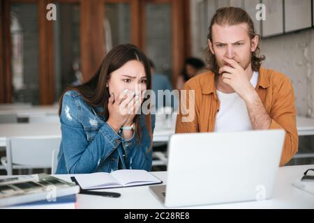 Porträt von Kollegen, die beim Arbeiten im Büro erstaunt auf einem Laptop blicken. Junge Studenten sitzen im Klassenzimmer und studieren zusammen mit Stockfoto