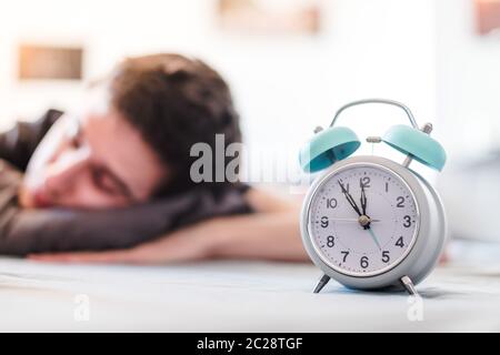 Wecker am Morgen. Junger Mann schläft im verschwommenen Hintergrund. Stockfoto