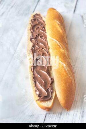 Die Hälfte der Baguette mit Schokoladencreme auf dem hölzernen Tisch Stockfoto