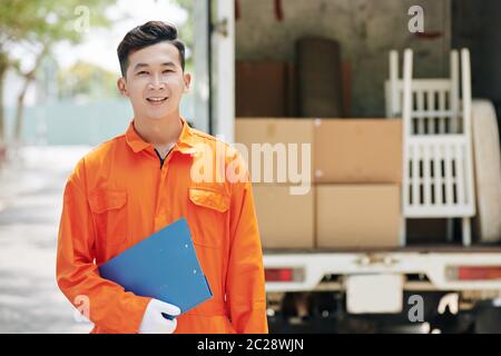 Horizontal Medium Porträt von jungen Erwachsenen asiatischen beweglichen Mann trägt leuchtend orange Uniform im Freien stehend hält blauen Zwischenablage, kopieren Raum Stockfoto