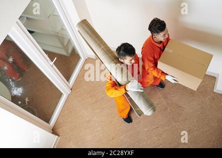 High-Angle-Ansicht Aufnahme von zwei beweglichen Männern tragen orange Uniform Teppich und Box mit Haushaltsgegenstand Stockfoto