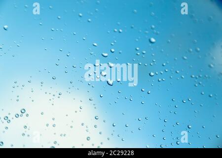 Wassertropfen auf dem Fenster, blauer Himmel und Wolken im verschwommenen Hintergrund. Stockfoto