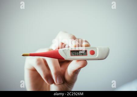 Der Mensch hält ein Rotfieber-Thermometer mit hoher Temperatur in der Hand Stockfoto