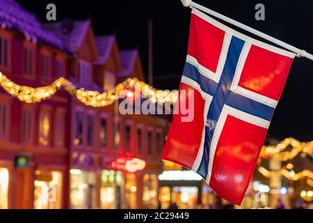 Norwegische Flagge an einem Pol in Tromso Zentrum in der Weihnachtszeit nach Einbruch der Dämmerung, Norwegen Stockfoto