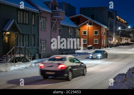 Autos fahren langsam und vorsichtig auf den rutschigen und bedeckt mit Schnee und Eis Wohnstraße in Tromso bei Dämmerung, Norwegen Stockfoto