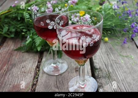 Mittsommernacht Traum Erdbeer Holunderflower Cocktail und wild blau und gelb Blumen auf dem Holzbrett Hintergrund. Zwei Gläser Rotwein Stockfoto