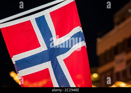 Norwegische Flagge an einem Pol in Tromso Zentrum in der Weihnachtszeit nach Einbruch der Dämmerung, Norwegen Stockfoto