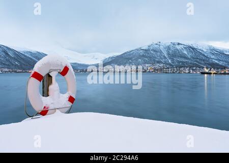 Rettungsring abgedeckt im Schnee am Ufer des berühmten tromso Brücke über Tromsoysundet Strait, Nördliches Norwegen Stockfoto
