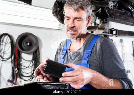 Ein Automechaniker, der einen alten, schmutzigen Ölfilter hält, der gerade aus einem Reparaturauto entfernt wurde Stockfoto