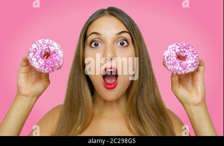 Überrascht junge Frau mit zwei Donuts in den Händen auf rosa Hintergrund. Stockfoto