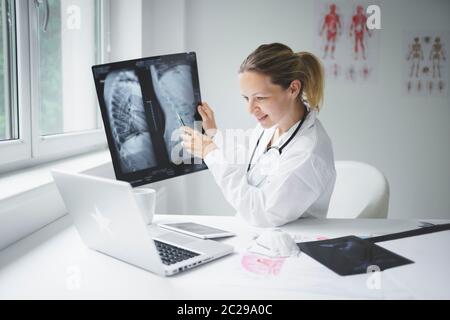 Hübsche und junge Ärztin diskutiert Röntgenbild online mit ihrem Patienten Stockfoto