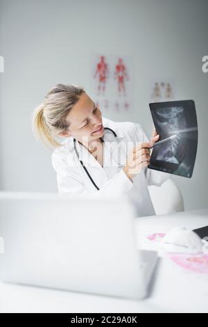 Hübsche und junge Ärztin diskutiert Röntgenbild online mit ihrem Patienten Stockfoto