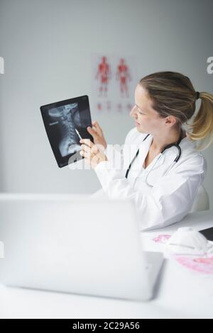 Hübsche und junge Ärztin diskutiert Röntgenbild online mit ihrem Patienten Stockfoto