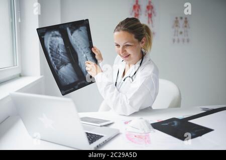 Hübsche und junge Ärztin diskutiert Röntgenbild online mit ihrem Patienten Stockfoto