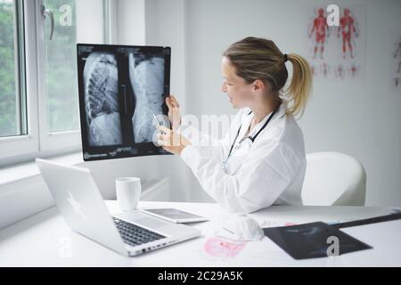 Hübsche und junge Ärztin diskutiert Röntgenbild online mit ihrem Patienten Stockfoto