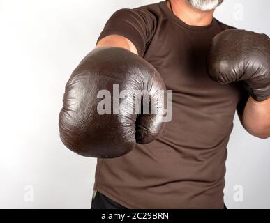 Mann steht in einem Rack, das Tragen von sehr alten Vintage Brown Boxhandschuhe auf seinen Händen, weißer Hintergrund Stockfoto