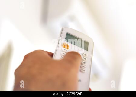 Nahaufnahme einer Hand, die die Temperatur der Klimaanlage mit der Fernbedienung anpasst Stockfoto