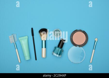 Feminine Beauty Care Flach von face makeup Blush, Bürsten, Nagellack und Glitter auf blauem Hintergrund, erhöhte Ansicht von oben, direkt über Stockfoto