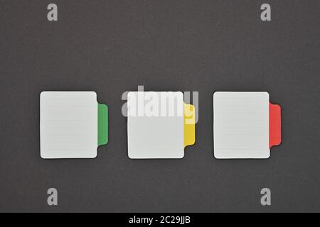 Schließen Sie die drei leeren weißen Papier mit bunten Labels über grauer Hintergrund Stockfoto