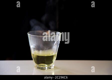 Rauch heißen chinesischen Tee auf einem transparenten Glas auf einem weißen Tisch auf einem schwarzen Hintergrund platziert. Stockfoto