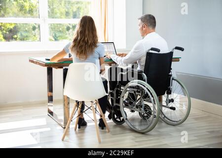 Deaktiviert Geschäftsmann sitzt mit seinem Partner mit Laptop über Schreibtisch im Büro Stockfoto