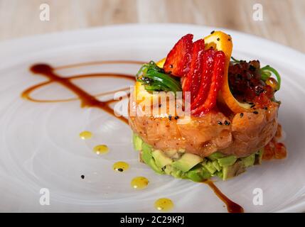 Lachs und Avocado-Tartare mit Wakame-Algen, Erdbeeren, Lumpfish-Rogen und mit einer Orangenscheibe verziert. Asiatische Küche. novelle Cousine Stockfoto